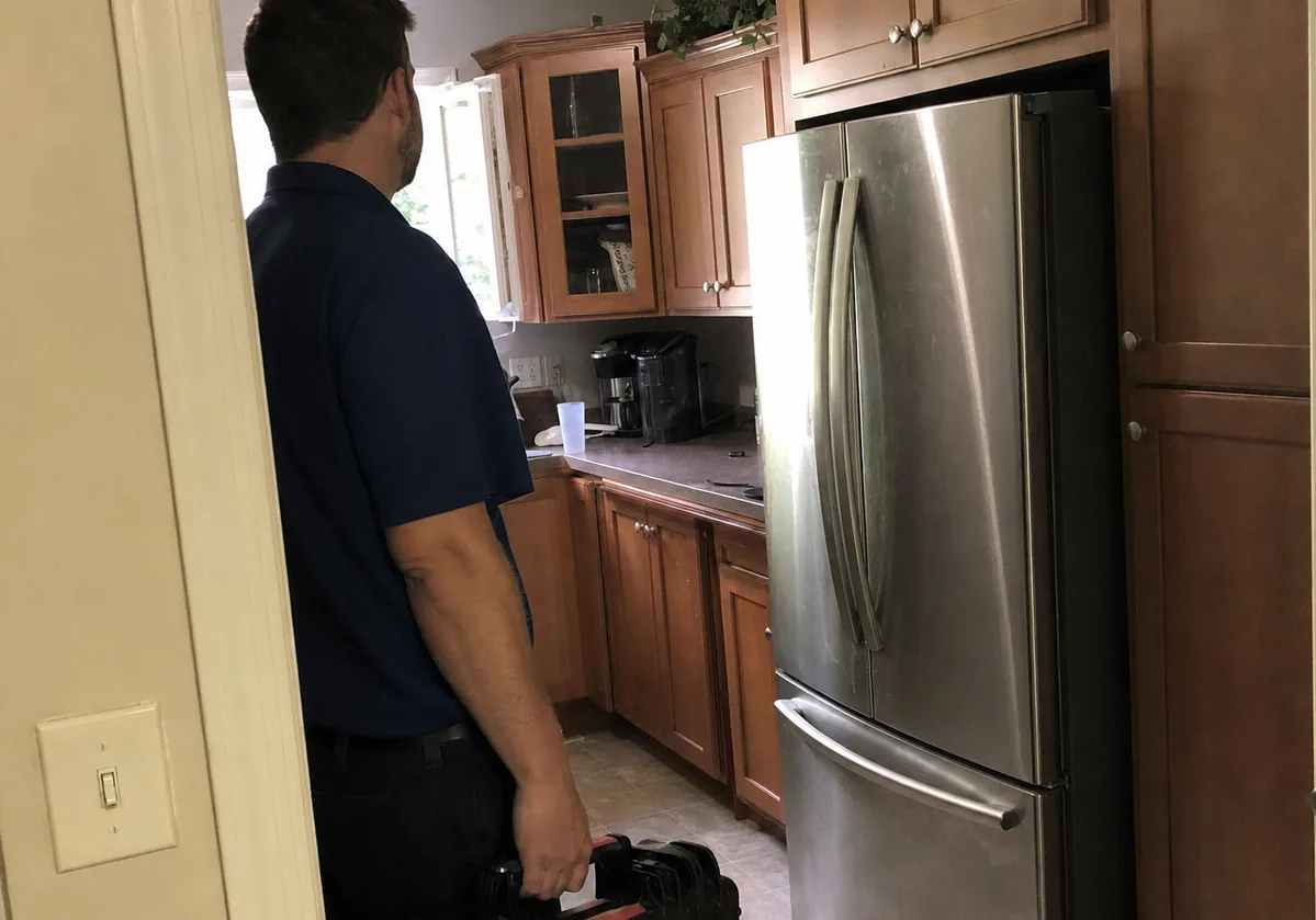 Centre of an arrival: the technician, the galley run of cabinets and the refrigerator column that fills the far wall